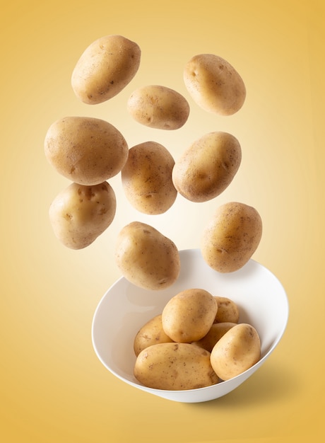 Potatoes flying over white bowl, isolated from brown background