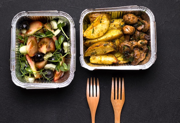 Potatoes and mushrooms in a container next to salad and cutlery. Home delivery concept