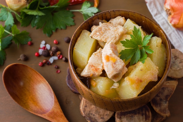 Potatoes stewed with chicken and vegetables in a wooden bowl.