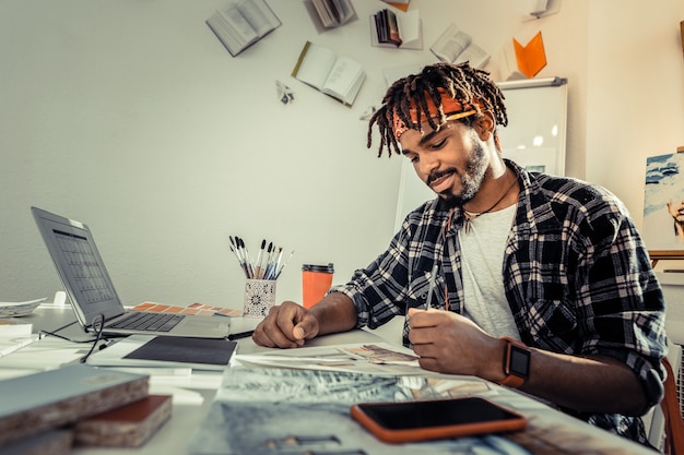 Foto potlood vasthouden. bebaarde donkerharige kunstenaar met dreadlocks die potlood vasthoudt tijdens het tekenen van schetsen