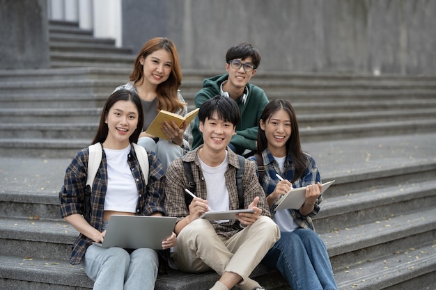 Potrait of young Asian college students working on group project while sitting on staircase of college campus