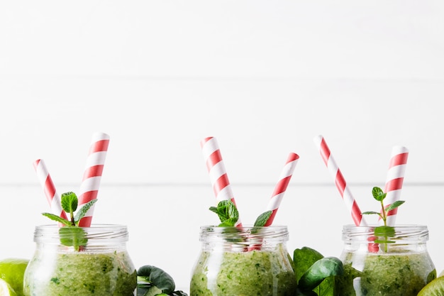 Potten met groene smoothie en rode buisjes op een lichte achtergrond.