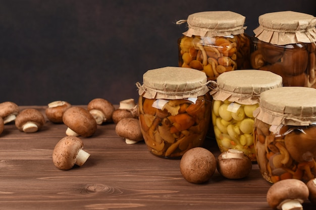 Potten met verschillende soorten paddenstoelen. Ingeblikte gemarineerde champignons in glazen potten. Geconserveerde champignons op houten tafel.