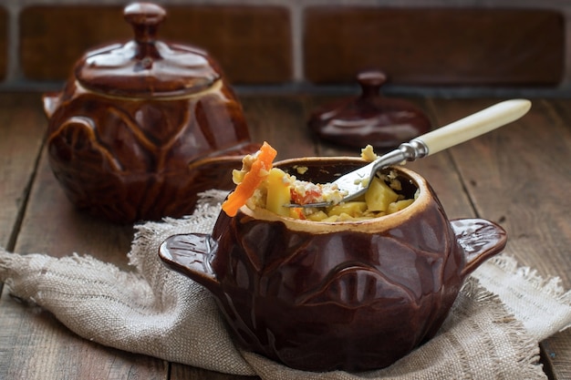 Potten van stoofpot kip aardappelen en groenten op houten ondergrond met linnen servet