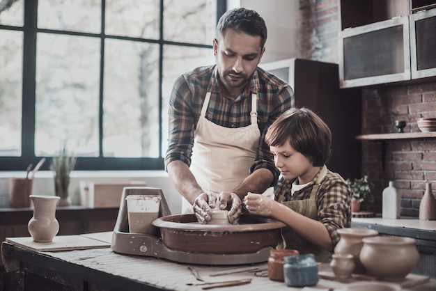 Pottenbakkerij met zoon. Zelfverzekerde jonge man en kleine jongen die keramische pot maken op de aardewerkklas