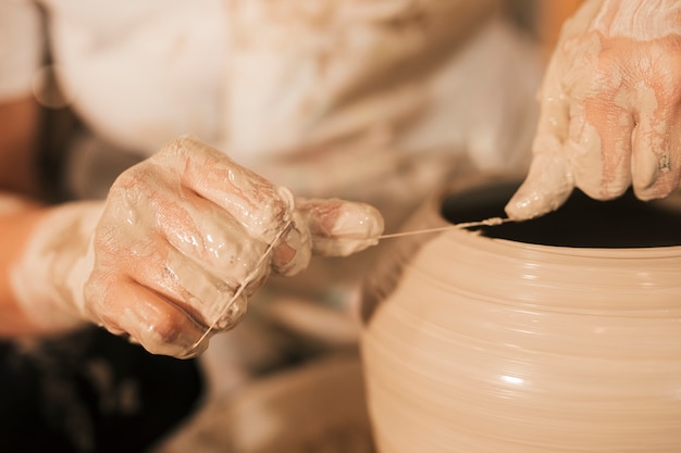 Photo potter cuts the edges of pottery with thread on spinning wheel