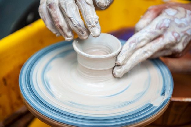 The potter makes pottery dishes on potter's wheel The sculptor in workshop makes clay product closeup Hands of the potter