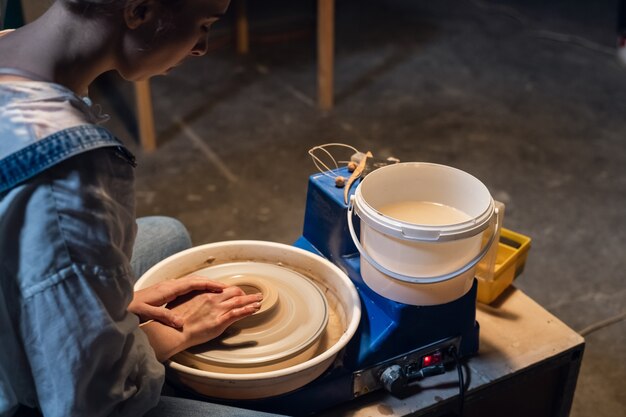 Photo on a potter's wheel, a young potter makes a preparation for a pot out of clay.