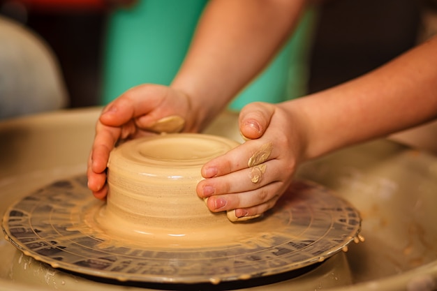 Potter teaching child to make ceramic pot on the pottery wheel