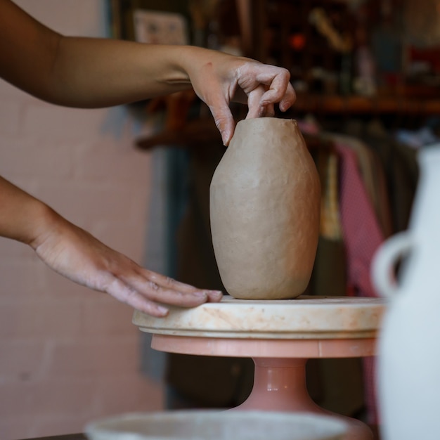 仕事で生の粘土の女の子の職人の彫刻陶器の花瓶を形作る陶器の作成の女性アーティスト