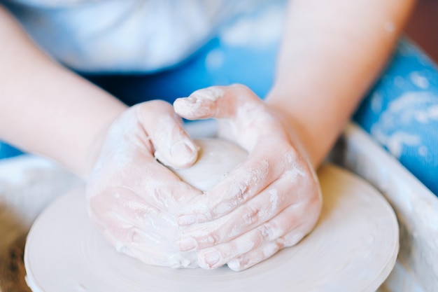 Mani di hobby dell'artigianato della ceramica che formano e modellano una palla di argilla sul tornio del vasaio