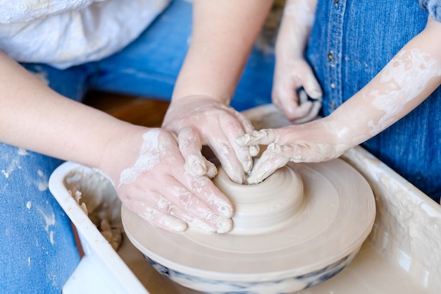Pottery handcraft hobby. two pairs of hands forming and shaping a ball of clay on potter wheel