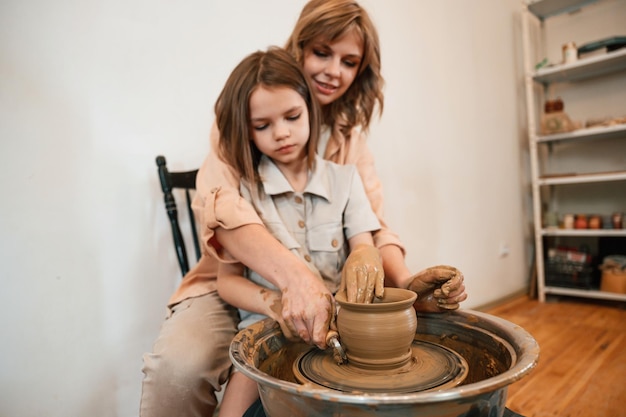 Pottery wheel Mother with little girl making ceramic pot in the workshop