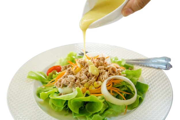 Pour cream mayonnaise on Tuna salad with fresh vegetable as Lettuce cucumber tomatoes white onion salad on white plate focus selective