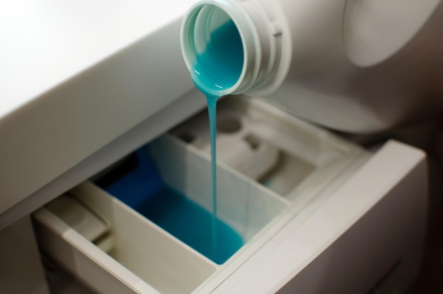 洗濯機の白いボトルに洗濯用のジェルを注ぎ、衣類を洗うための青いジェルを入れます。