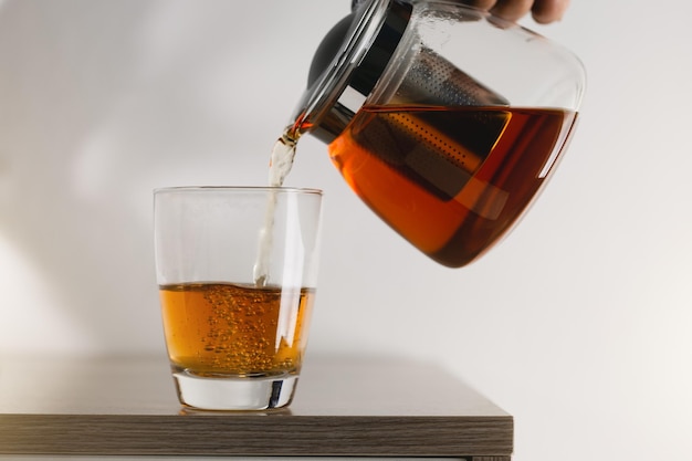 Pour hot tea into a glass clear placed on a wooden table