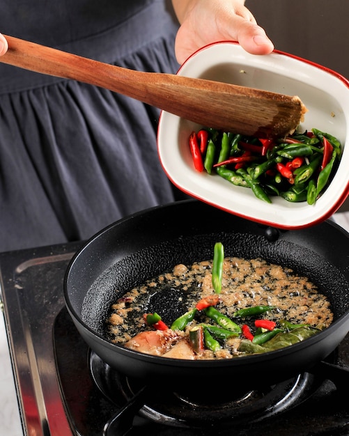 スパイスを炒める前に、刻んだ赤と緑の唐辛子を鍋に注ぐか入れます。アジアの伝統的な料理を作るキッチンでの調理プロセス
