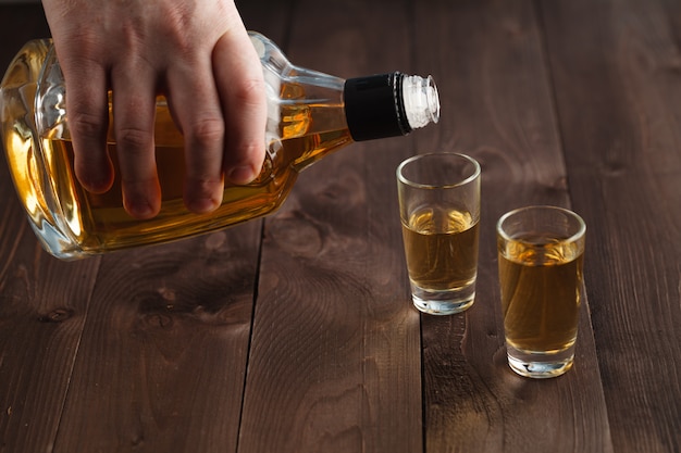 Pouring alcohol in shot glass on wooden table