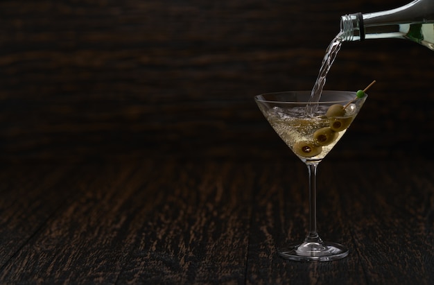 Pouring alcoholic beverage from the bottle into the glass against wooden table.