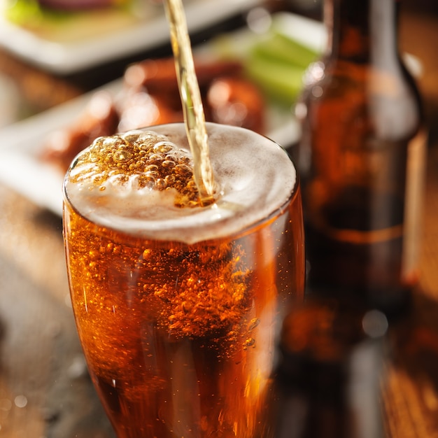 Photo pouring beer into a glass with barbecue chicken wings