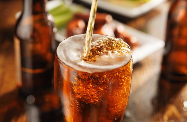 Pouring beer into glass with barbecue chicken wings