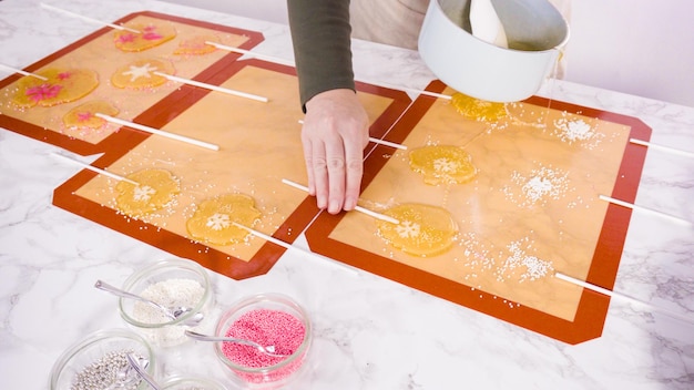 Pouring caramelized sugar on silicone mats to make homemade lollipops.