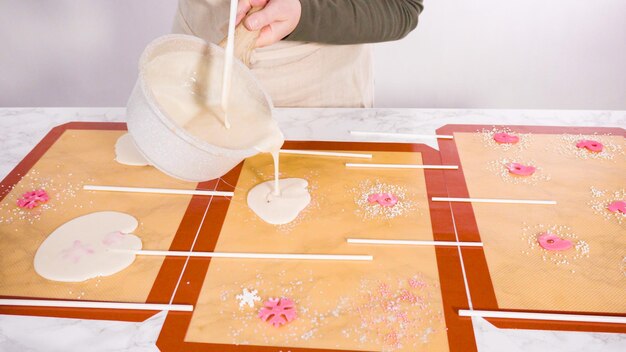 Pouring caramelized sugar on silicone mats to make homemade lollipops.