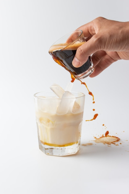 Pouring coffee into cup ice milk on white background.