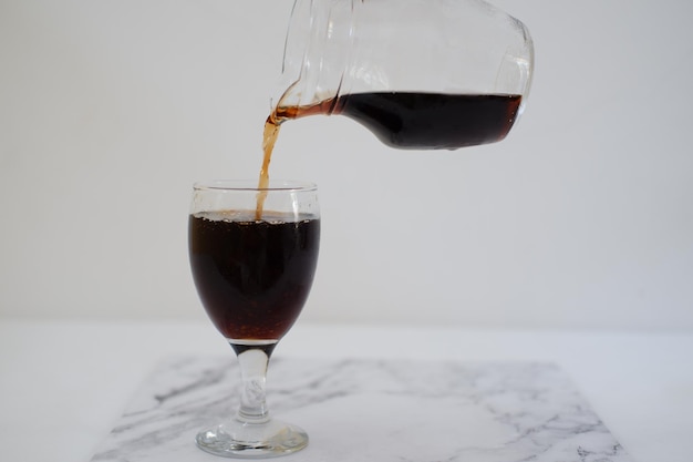 Pouring cola from a jug into a glass on a white background