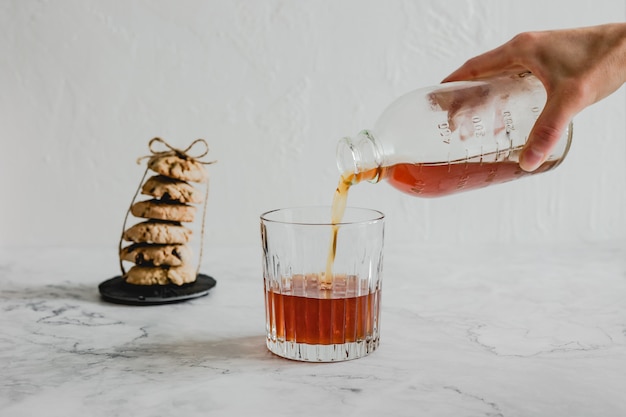 Pouring cold brew coffee into a glass, a stack of oatmeal cookies