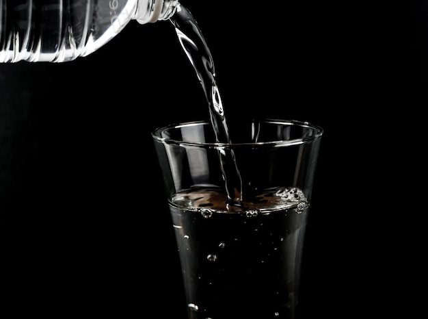 Pouring fresh water on glass on black background.