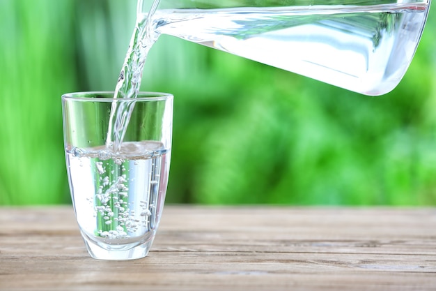 Pouring of fresh water into glass on table outdoors