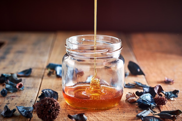 Pouring golden honey in the glass jar on wooden table