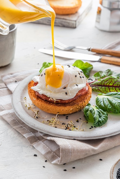 Pouring Hollandaise sauce over poached egg for cooking benedict egg for tasty breakfast vertical orientation