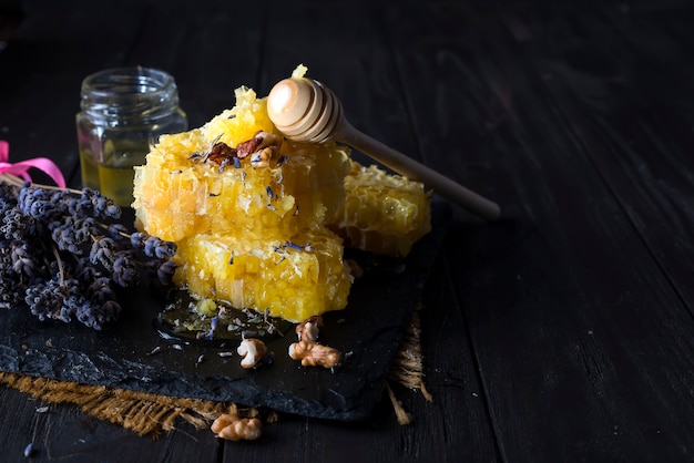 Pouring honey into honey comb with walnuts and lavender flowers on stone dark background