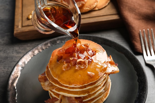 Photo pouring honey onto pancakes with bacon on plate