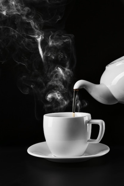 Foto versare il tè caldo da un bollitore in una tazza su sfondo nero da vicino