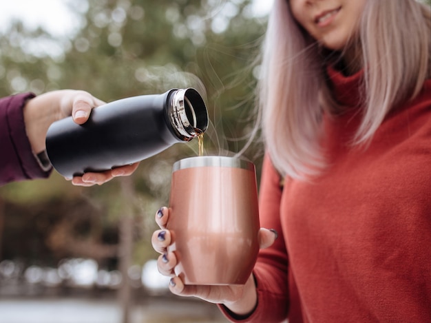 Photo pouring hot tea in a thermo mug with winter forest