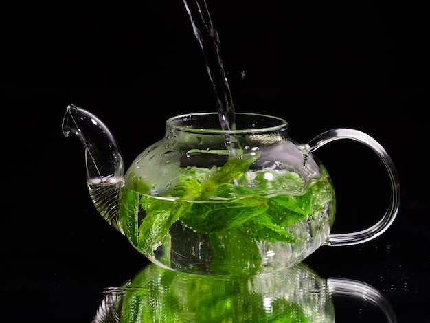 Pouring hot water into a glass teapot on a black background green mint tea herbal tea and healthy