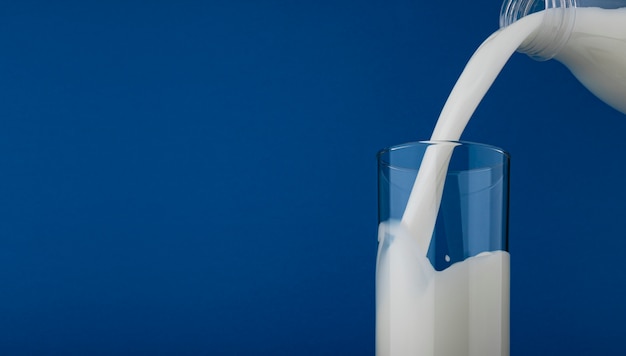 Photo pouring milk in glass isolated on blue background