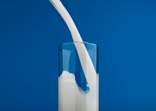 Photo pouring milk in glass isolated on blue wall