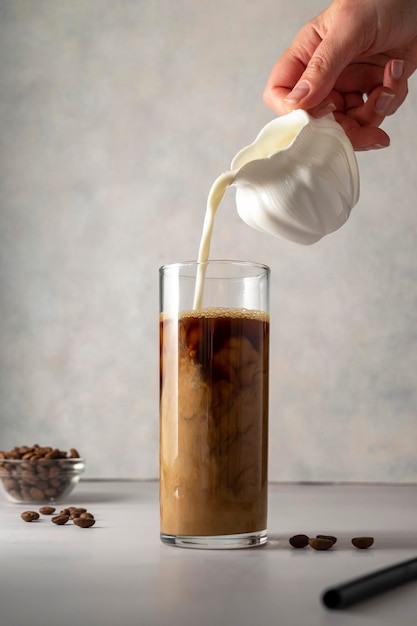 Pouring milk in glass with iced coffee Cold refreshment summer sweet drink