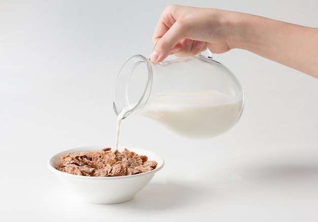 Pouring milk into the bowl with multigrain natural flakes on a white background Healthy food