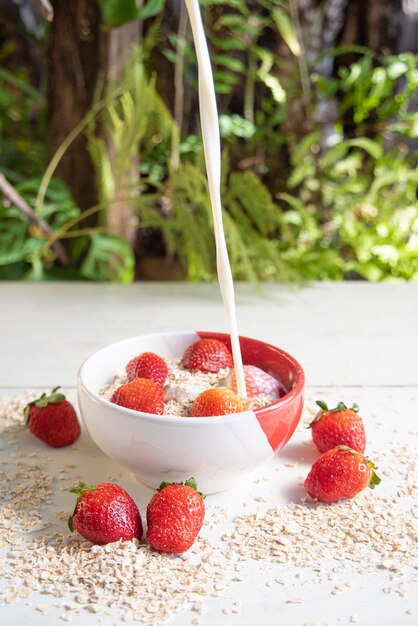 pouring milk into a bowl with oatmeal and strawberries