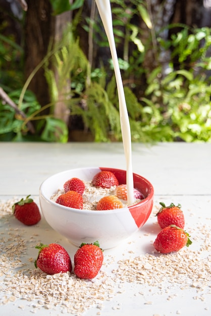 pouring milk into a bowl with oatmeal and strawberries