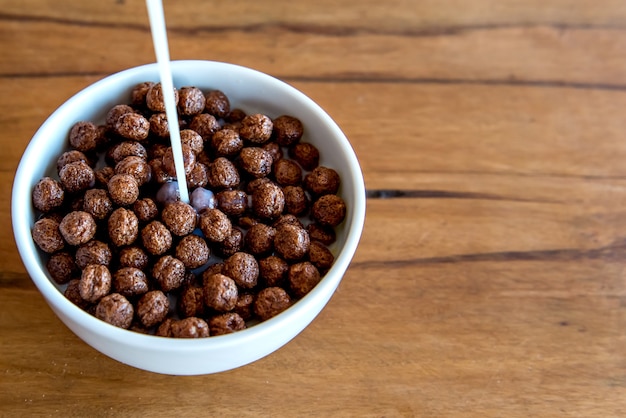 Pouring milk into chocolate cornflakes balls Breakfast with milk and cornflakes.