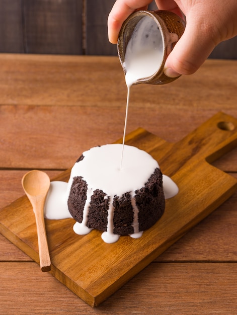 Foto versando la salsa di latte sui brownie al cioccolato sul piatto di legno e sullo sfondo di legno. prodotti da forno e dolci fatti in casa