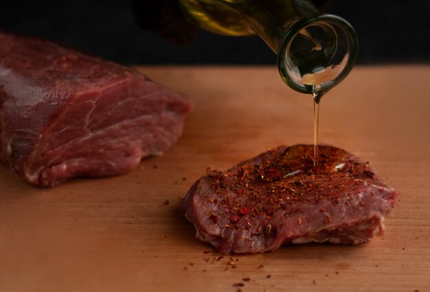 Photo pouring oil on beef steak with spices on a wooden board