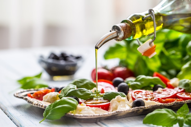 Pouring olive oil on caprese salad. Healthy italian or mediterranean meal.