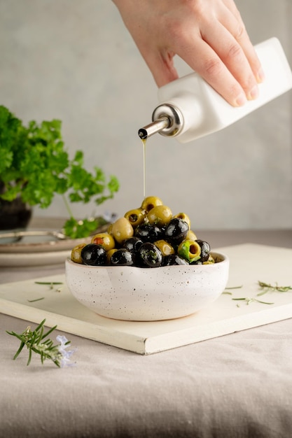 Pouring olive oil over green and black olives in a bowl